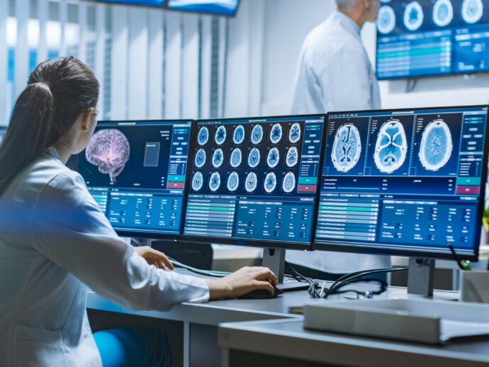 Team of Professional Scientists Work in the Brain Research Laboratory. Neurologists / Neuroscientists Surrounded by Monitors Showing CT, MRI Scans Having Discussions and Working on Personal Computers.