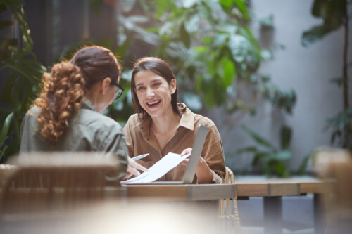 Two Smiling Young Women Discussing Business Project in Cafe