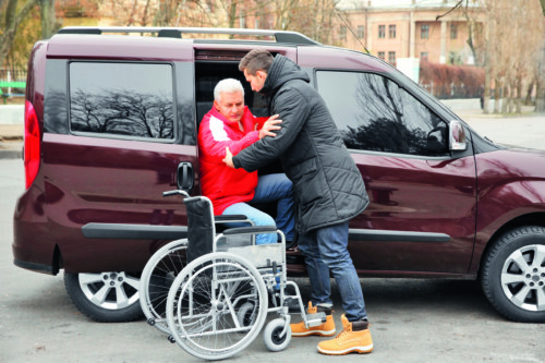 Young man helping handicapped man to sit in wheelchair