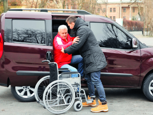 Young man helping handicapped man to sit in wheelchair