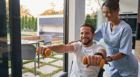 Woman nurse assistant helping to the man with a physical disability in the modern apartments