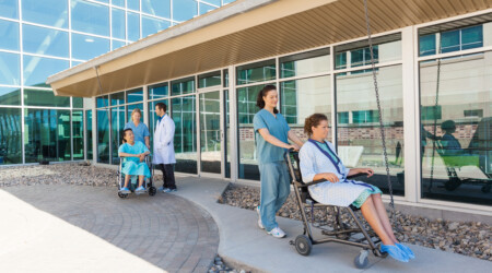 Medical Team With Patients On Wheelchairs At Hospital Courtyard