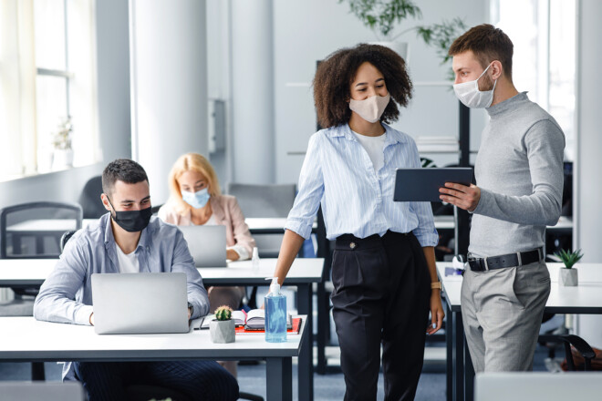 New project and plans for work. Boss in protective mask with tablet gives instructions to workers in masks, african american woman looking at gadget