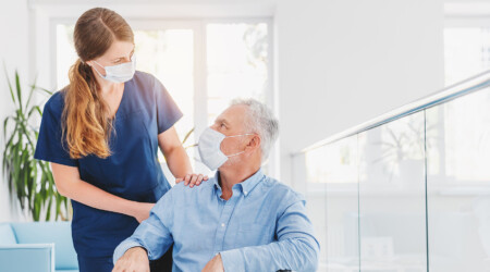 Young woman nurse explaining information to man patient in wheelchair in medical face mask while talking together in hospital. Epidemic and virus concept