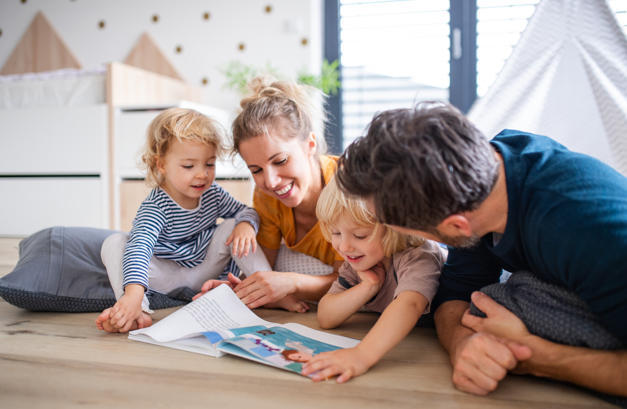 Famille avec deux adultes et deux enfants dans une chambre, lisant un livre
