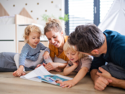 Famille avec deux adultes et deux enfants dans une chambre, lisant un livre