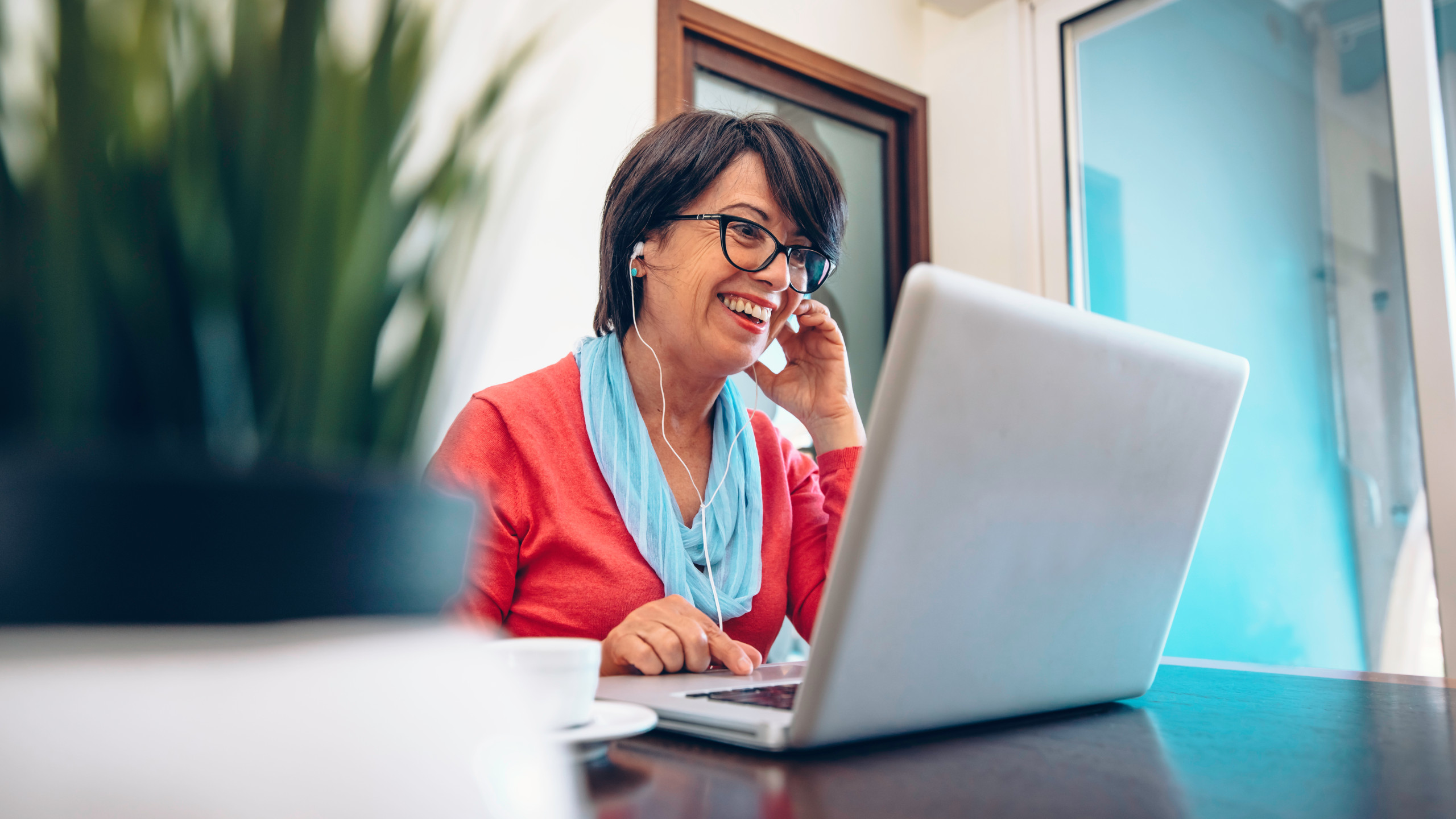 Sixty year old female teacher wearing headphones having online c