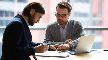 Focused young businessman signing agreement with skilled lawyer.