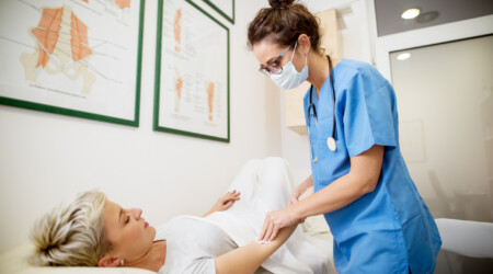 Close up portrait view of middle aged professional nurse holding hands with a patient while woman patient lying on the bed in front.