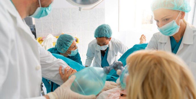 Group of medical professionals helping pregnant woman to deliver baby, giving her oxygen and encouraging her in hospital delivery room. Medical team and pregnant woman in labor.