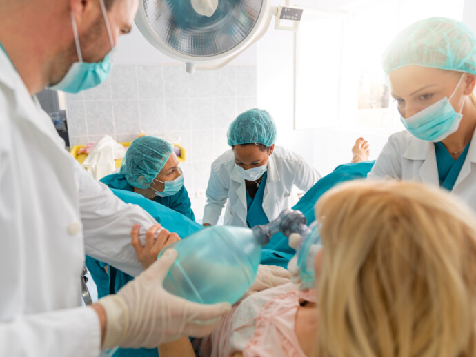 Group of medical professionals helping pregnant woman to deliver baby, giving her oxygen and encouraging her in hospital delivery room. Medical team and pregnant woman in labor.