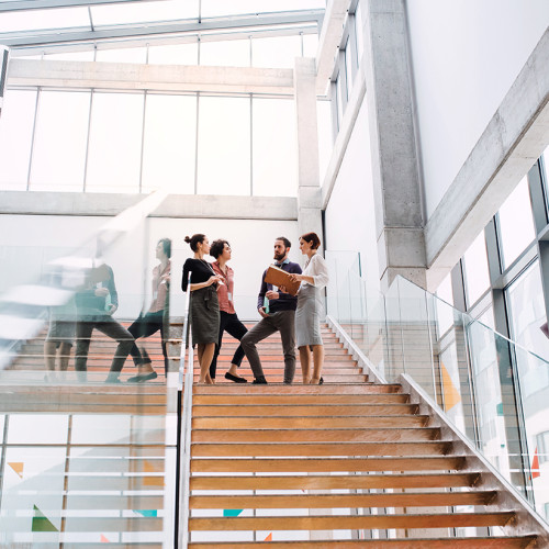 Group of young businesspeople standing on a staircase, talking.