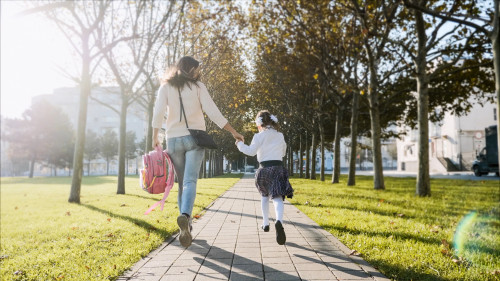 A woman and little girl in school uniform running in park, back view
