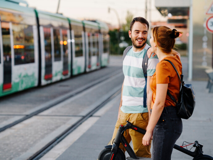 Couple with folded electric scooter waiting at tram stop