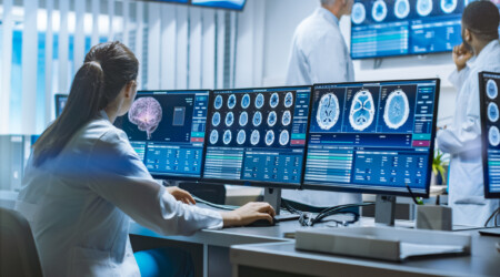 Team of Professional Scientists Work in the Brain Research Laboratory. Neurologists / Neuroscientists Surrounded by Monitors Showing CT, MRI Scans Having Discussions and Working on Personal Computers.