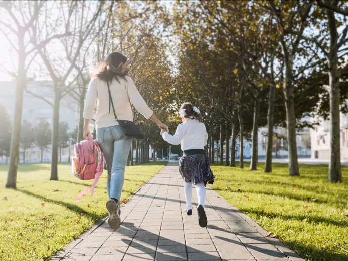 A woman and little girl in school uniform running in park, back view