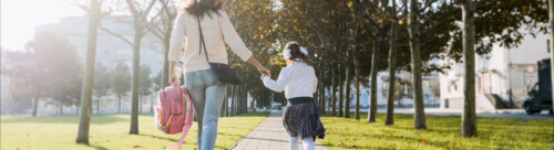 A woman and little girl in school uniform running in park, back view