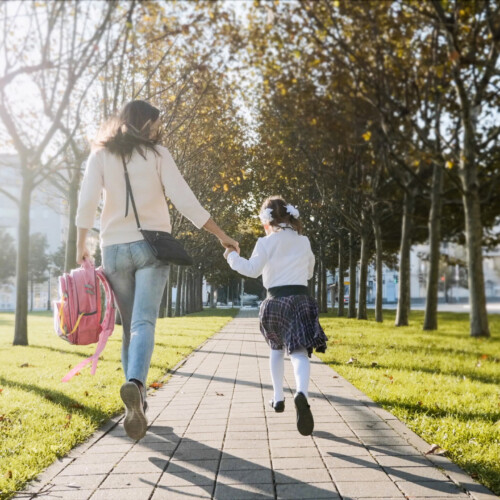 A woman and little girl in school uniform running in park, back view