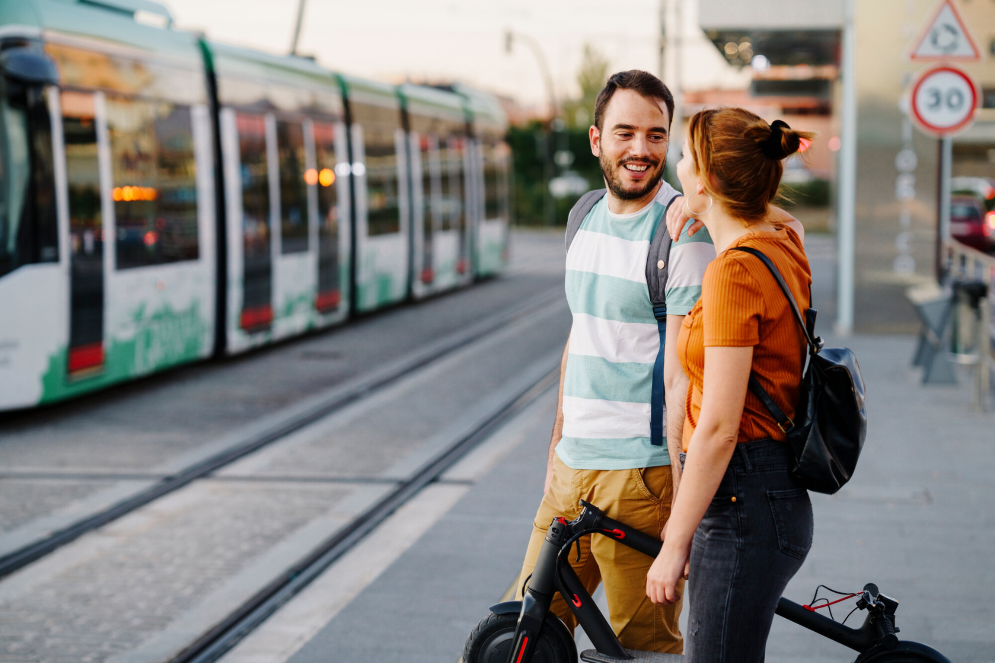 Couple with folded electric scooter waiting at tram stop