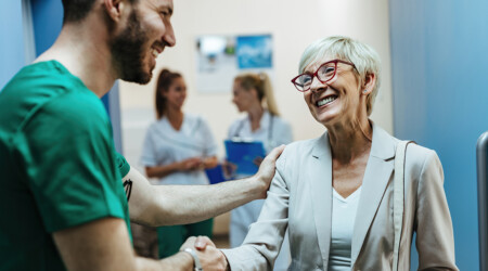 Happy senior woman shaking hands with a surgeon in a hospital ha