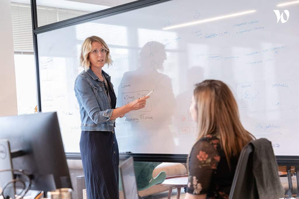 Collaboratrice faisant une présentation ou une session de travail devant un tableau blanc.