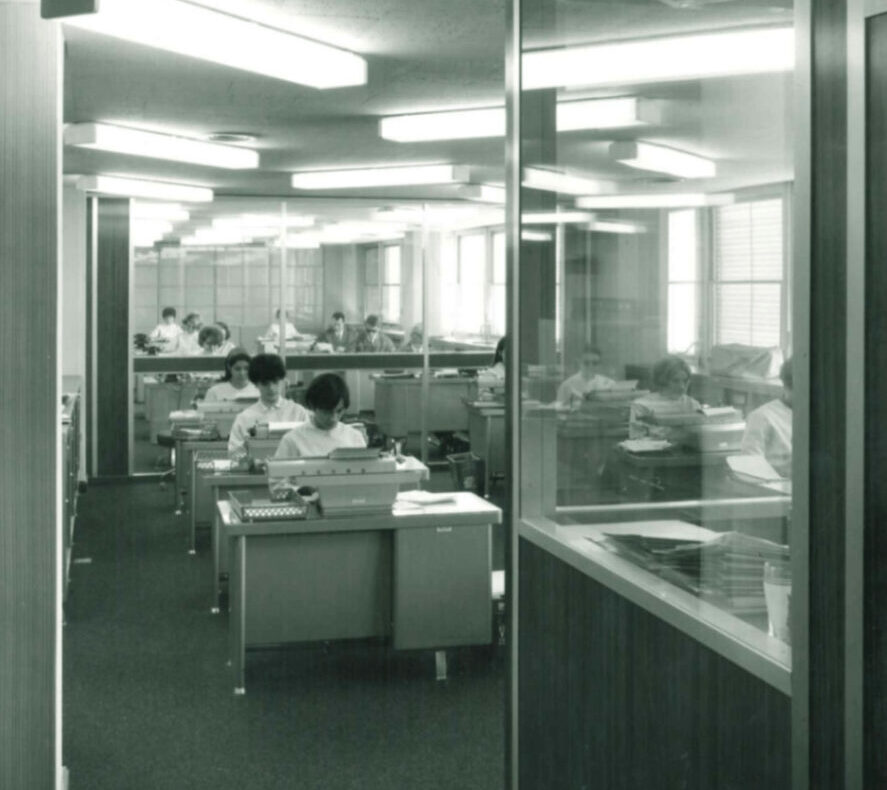 Bureau des années 60 avec employés travaillant sur des machines à écrire.