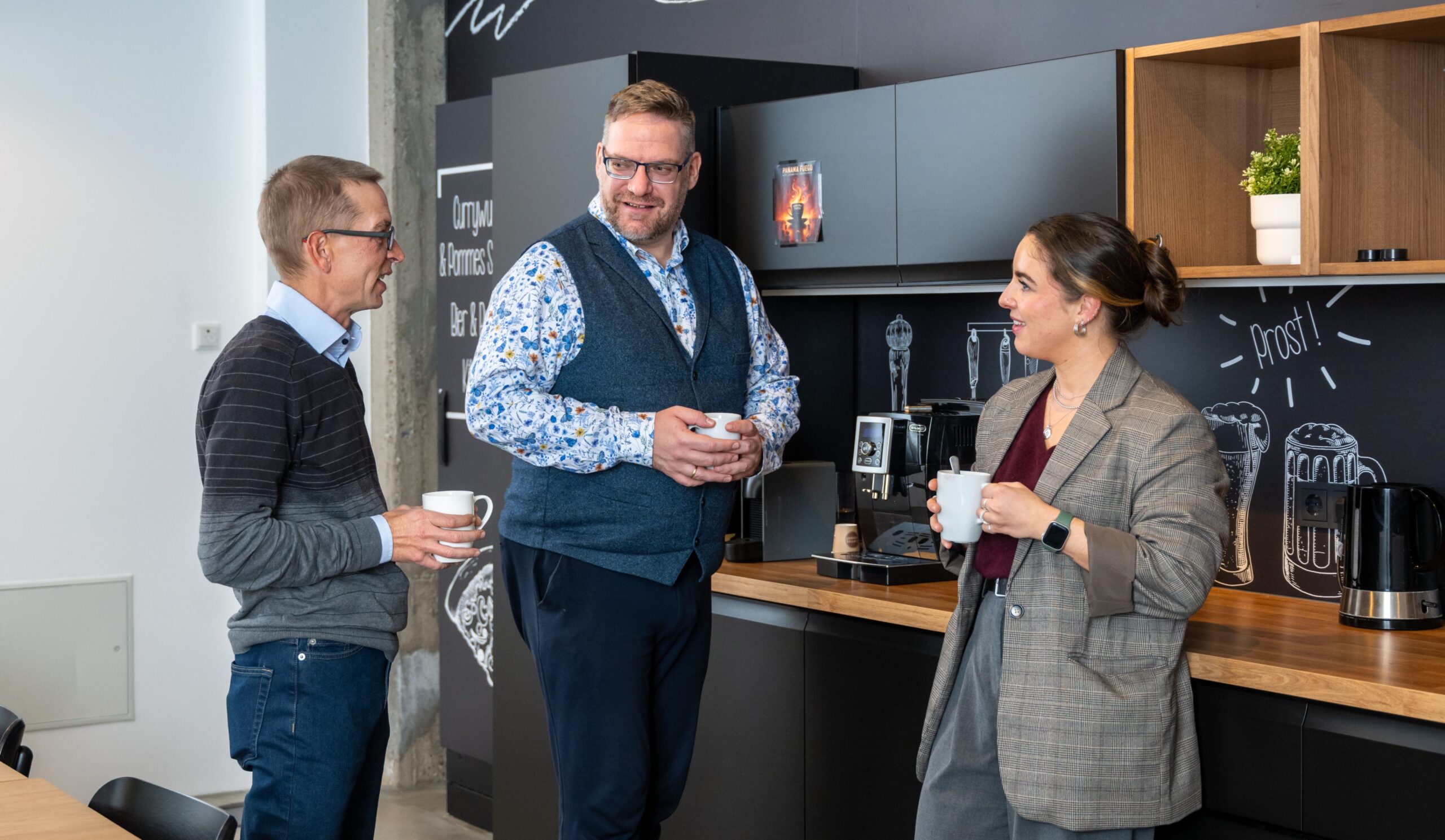 Mitarbeitende unterhalten sich bei einer Kaffeepause in der Büroküche.
