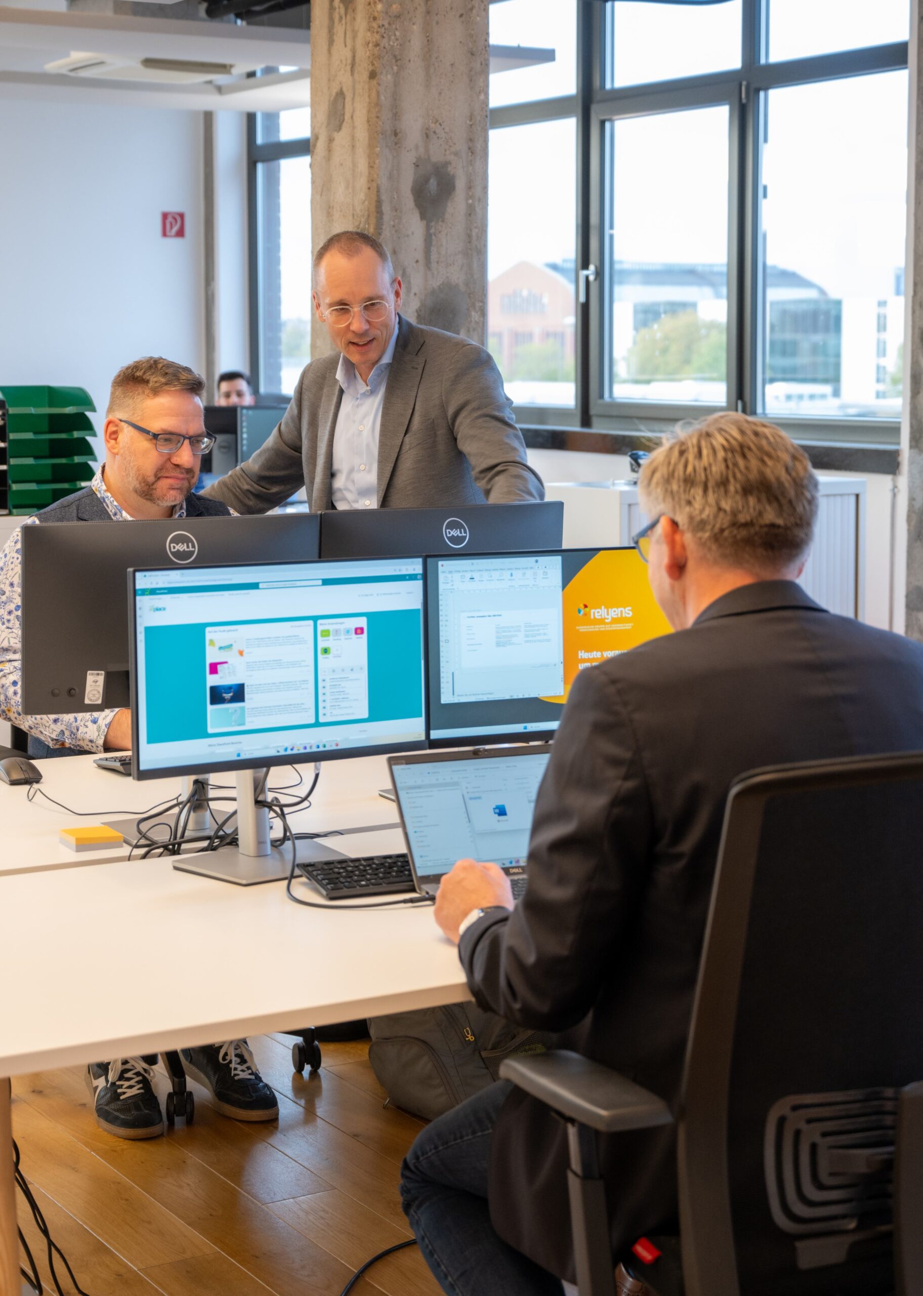 Mitarbeitende tauschen sich an ihren Schreibtischen in einem modernen Büro aus.