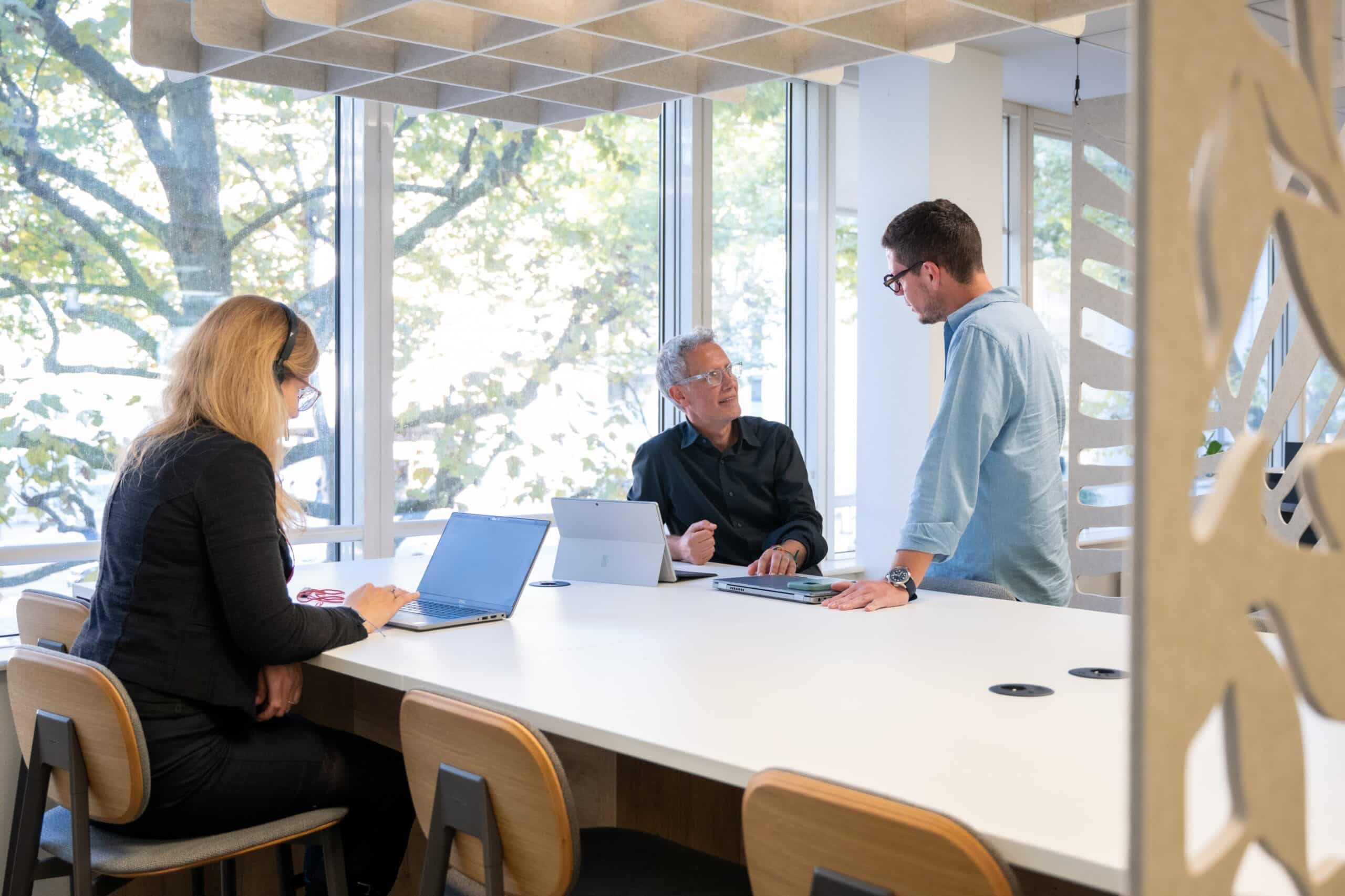 Trois collègues en discussion autour d’une grande table dans un espace de travail