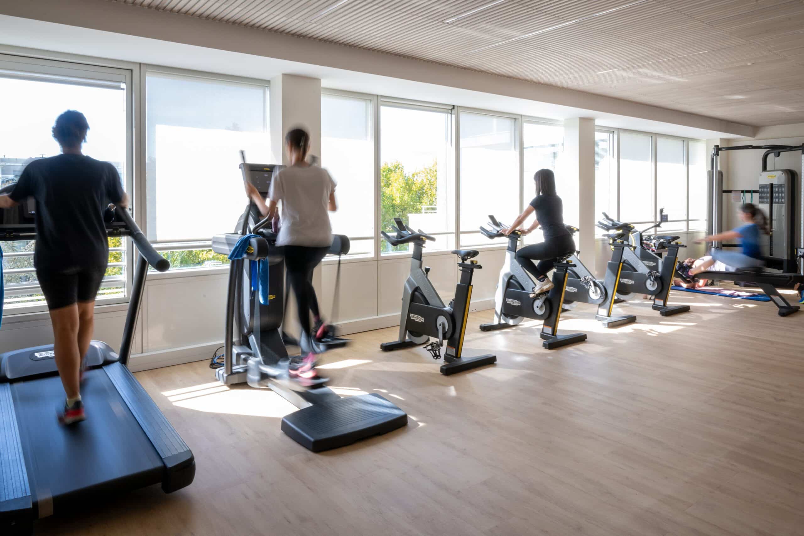Personnes s’entraînant sur des appareils de cardio dans une salle de sport lumineuse