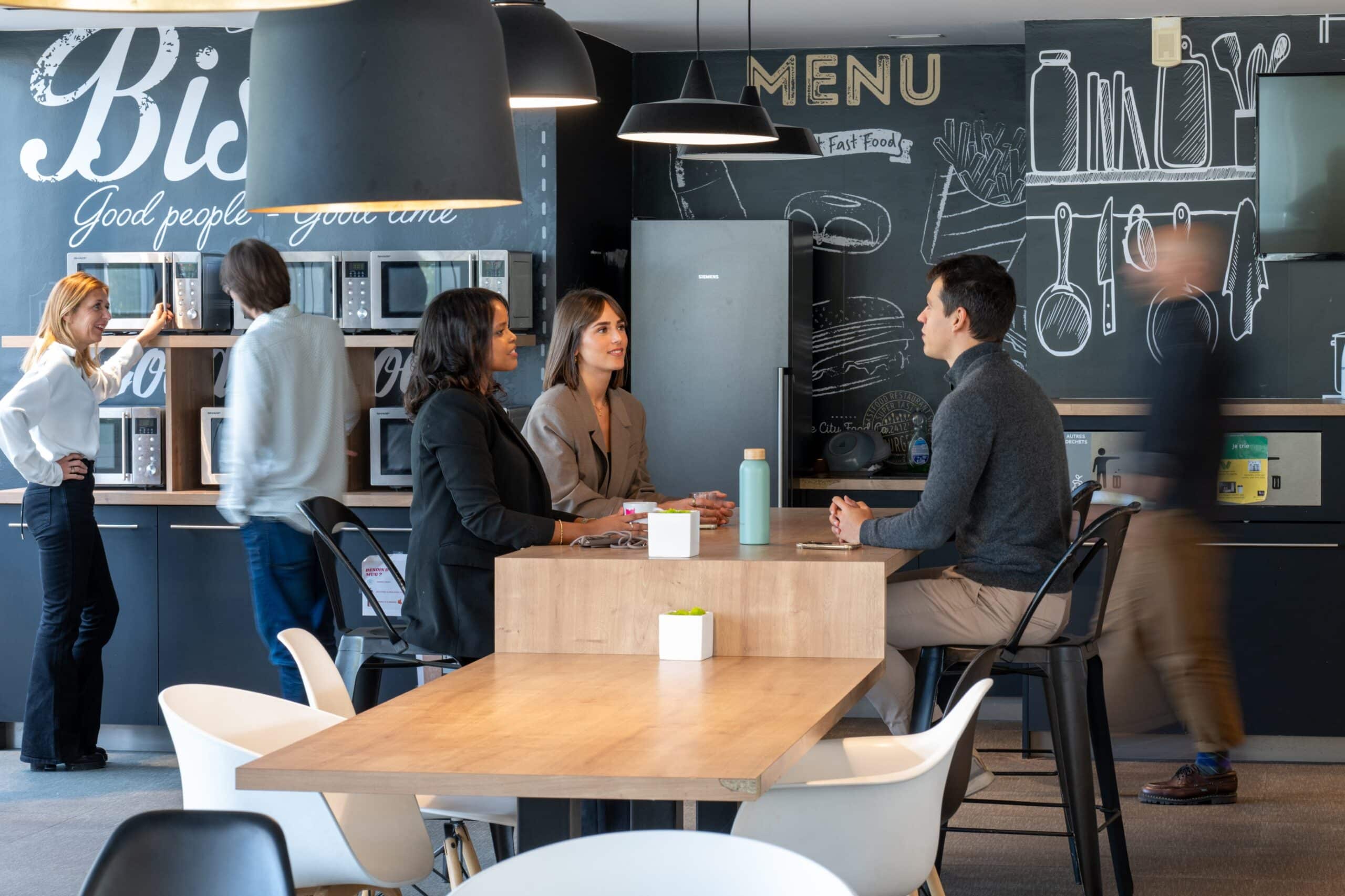 Collaborateurs échangeant et déjeunant dans un espace cafétéria convivial.