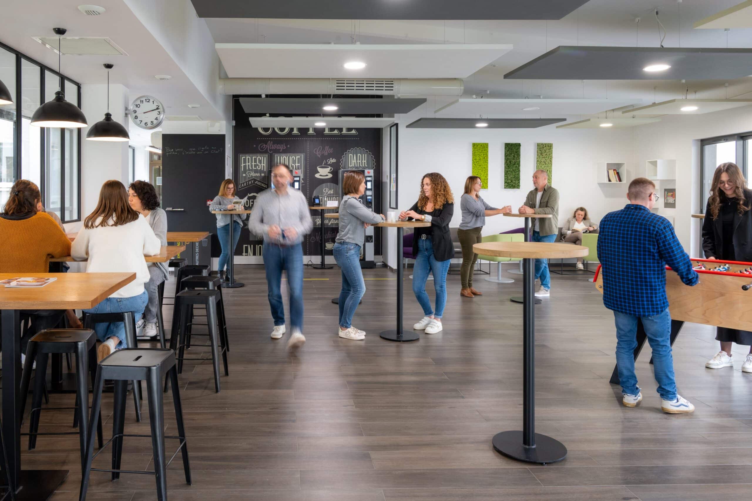 Espace détente où plusieurs collègues échangent, prennent un café ou jouent au baby-foot.