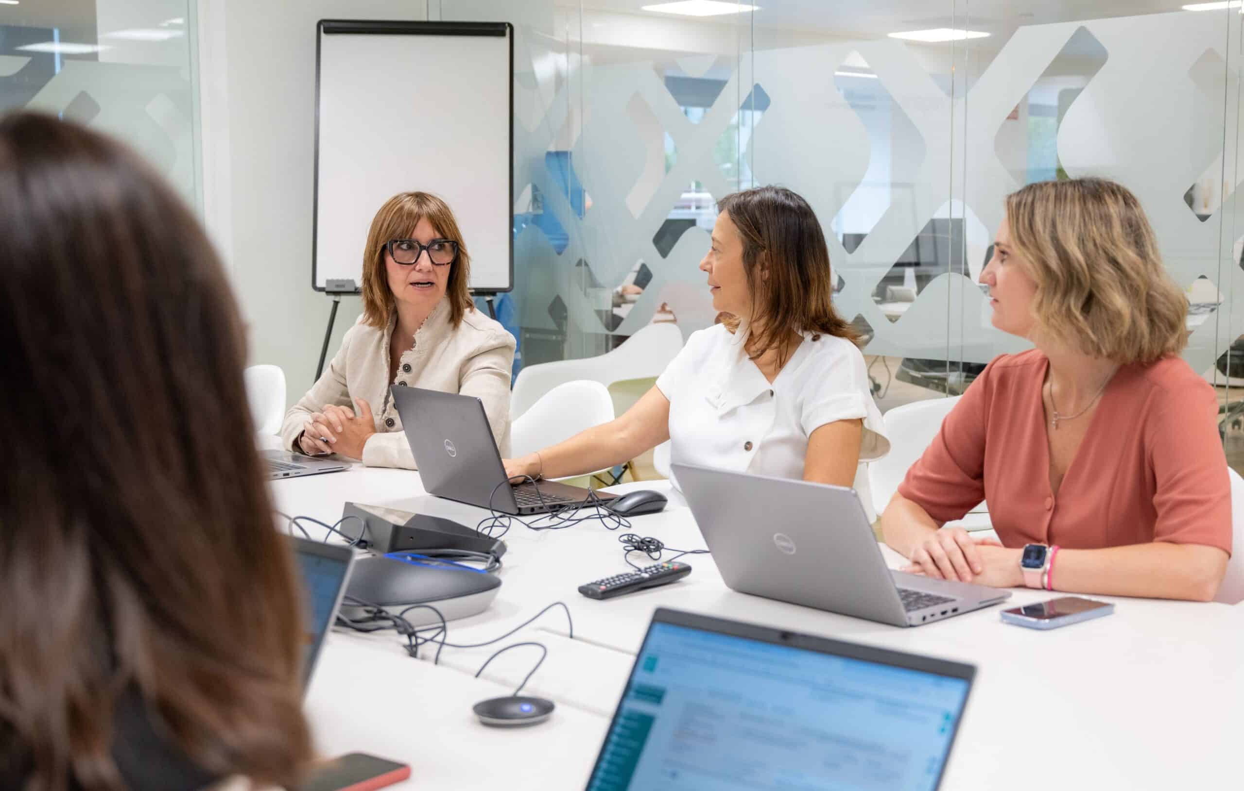Dos colaboradoras sonrientes mirando juntas la pantalla de un teléfono móvil.
