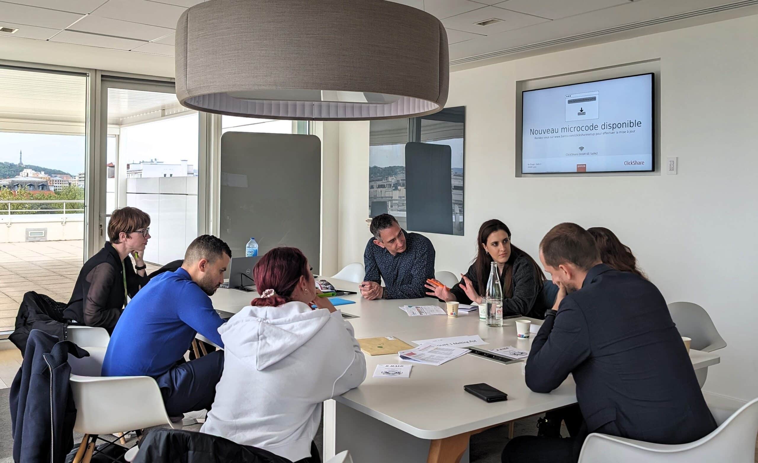 Groupe de collaborateurs en réunion autour d’une table dans une salle lumineuse.
